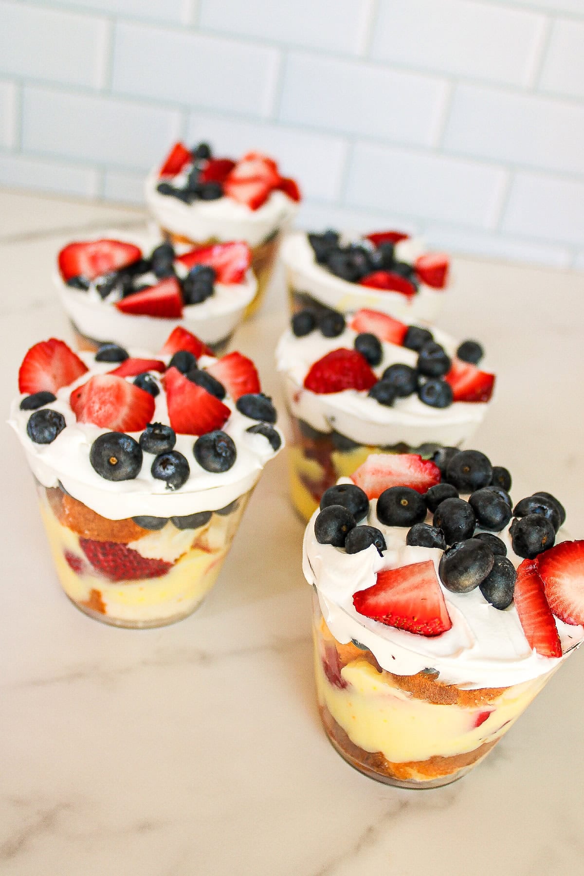 Finished parfait cups with layers of cake, vanilla pudding, strawberries, blueberries, and whipped topping.