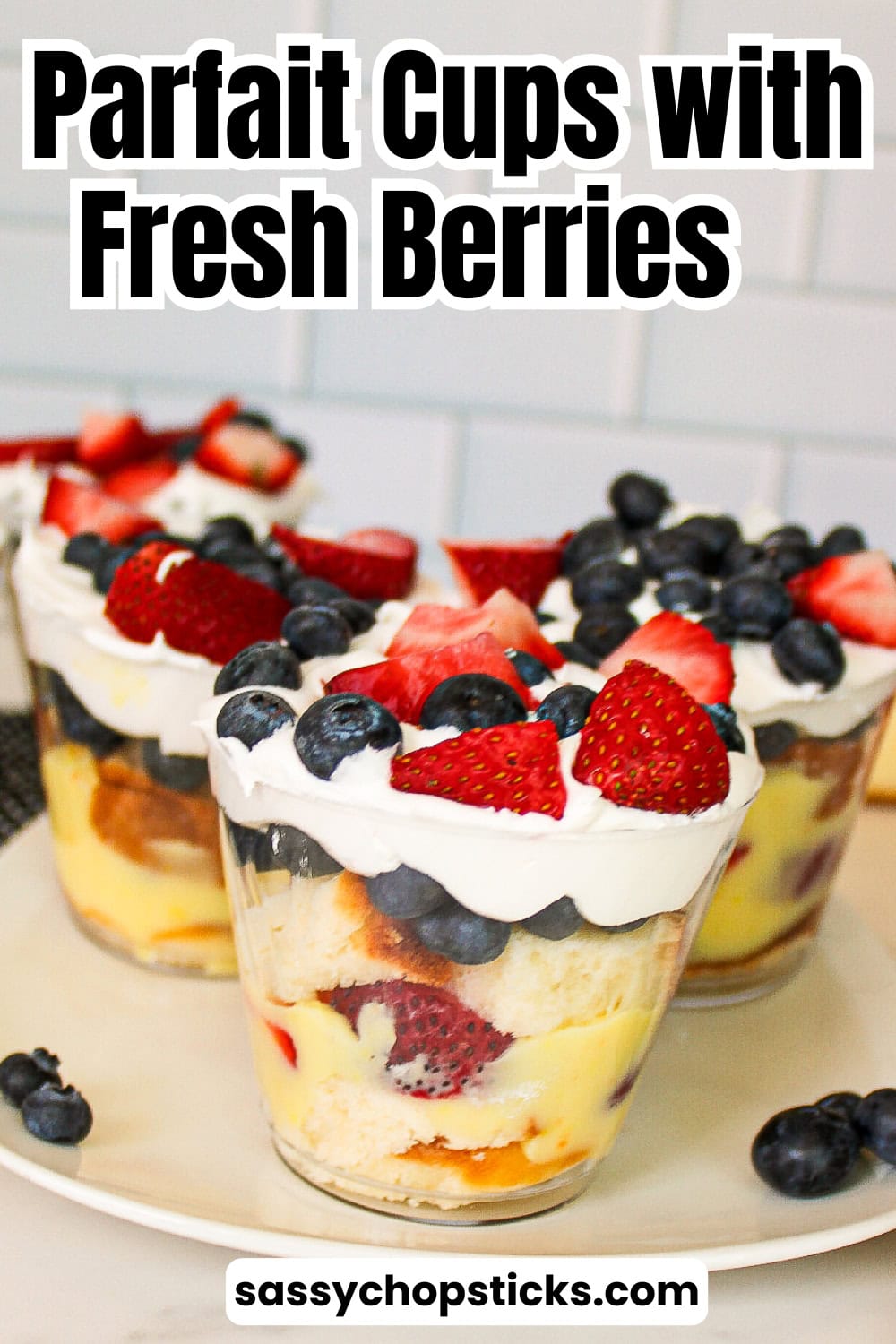 Parfait cups with fresh strawberries, blueberries, vanilla pudding, whipped topping, and cake layered in clear dessert cups on a white plate.