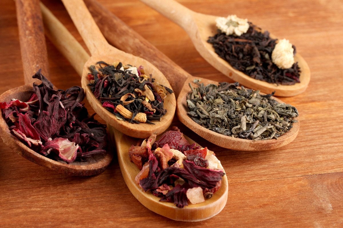 Assorted Chinese tea leaves displayed in wooden spoons on a wooden table.