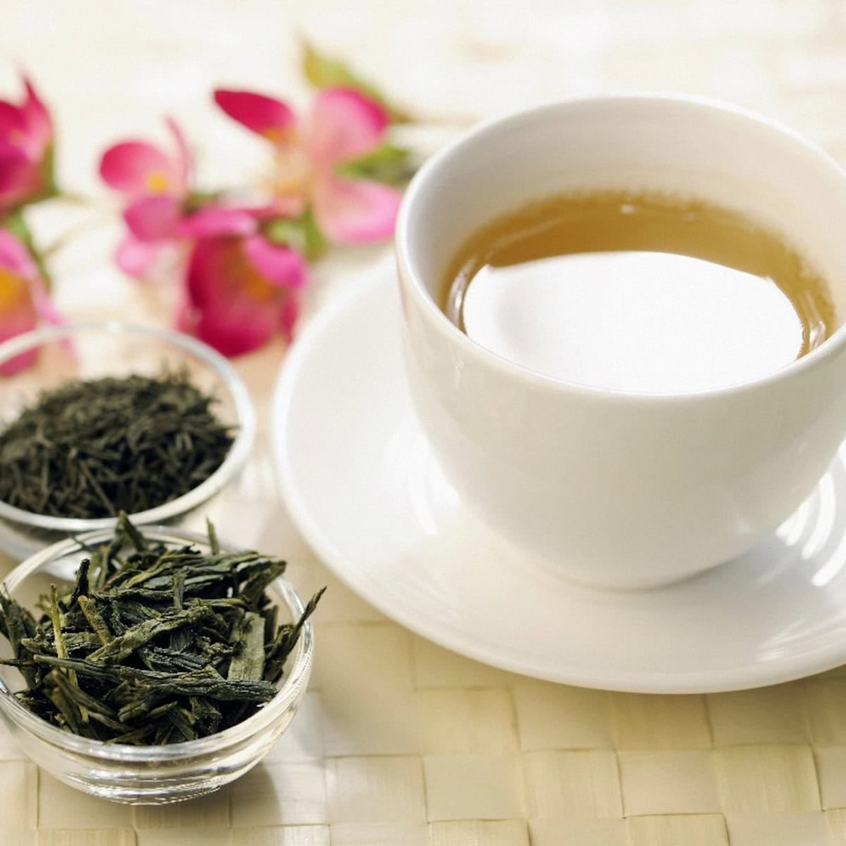 Cup of Chinese green tea with loose tea leaves and pink flowers beside it.