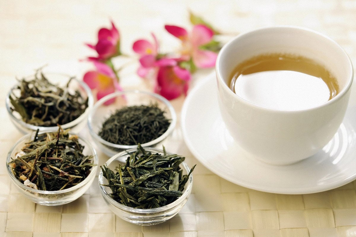 Chinese tea cup with assorted loose tea leaves and floral accents on a light background.