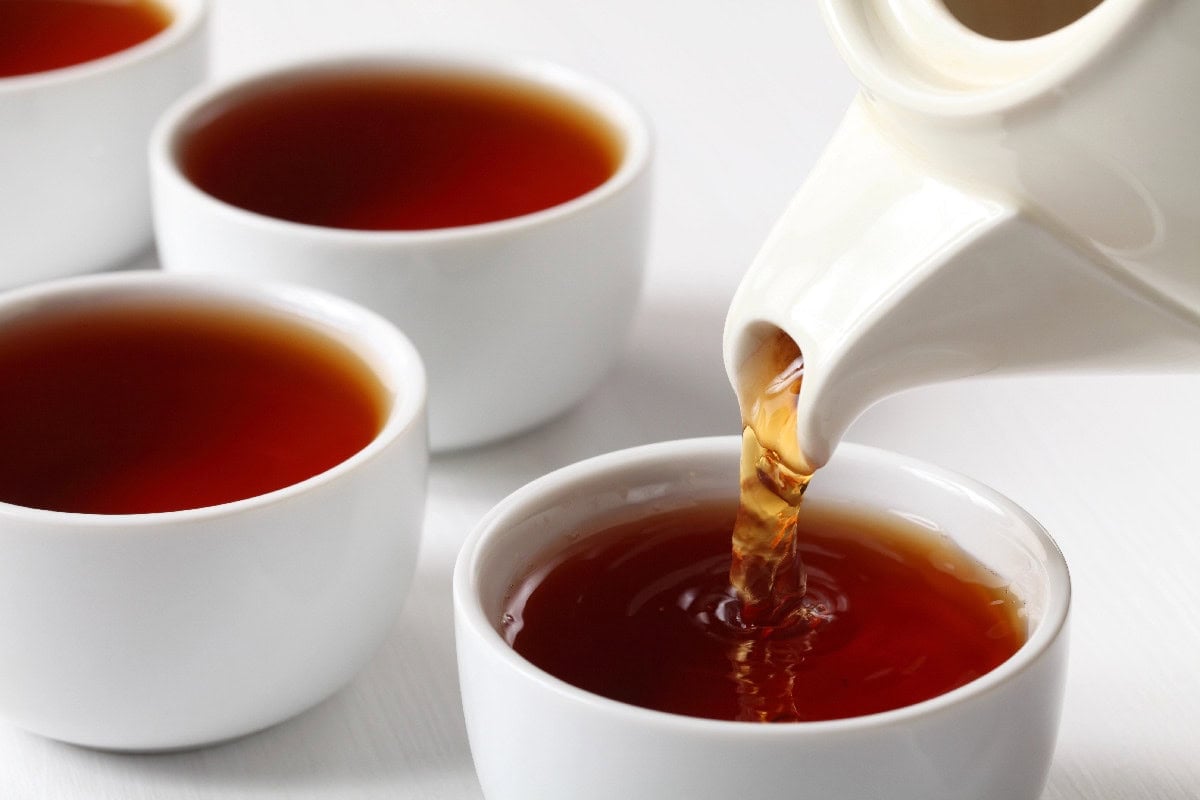 Pouring hot black tea into white teacups.