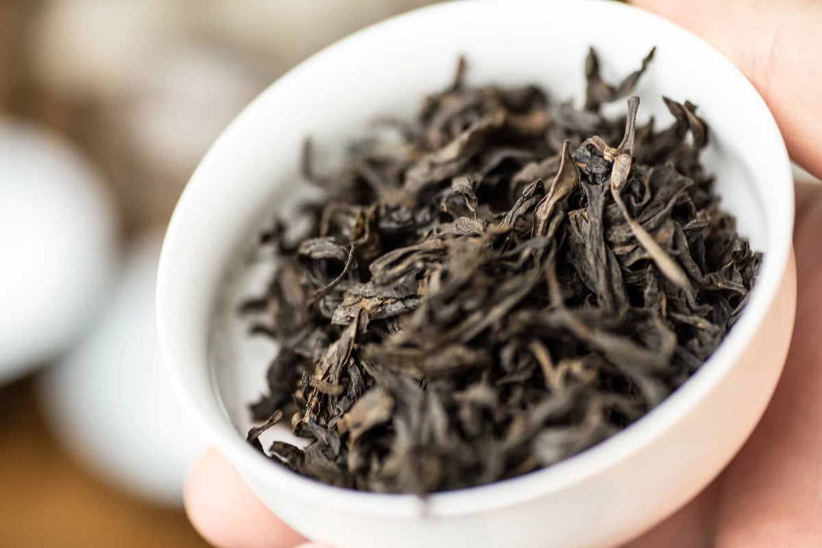 Close-up of loose oolong tea leaves in a white bowl.