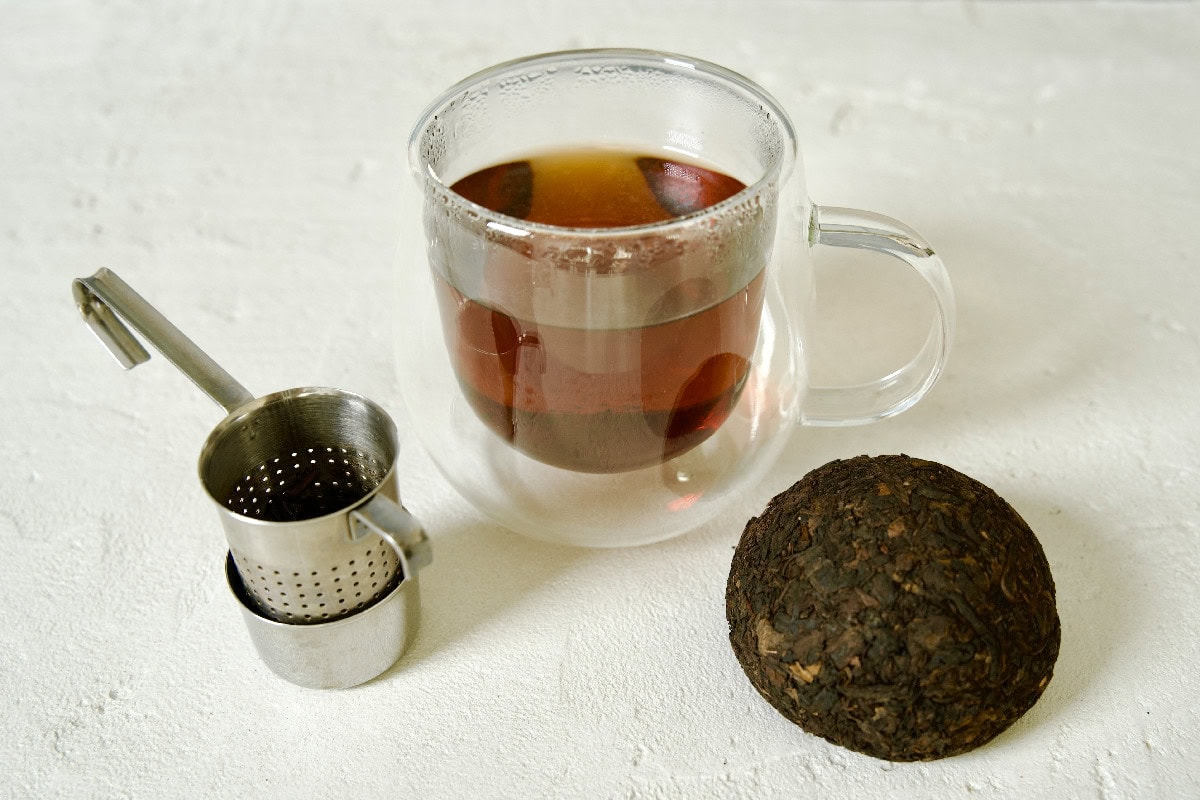 Glass cup of pu-erh tea with compressed tea cake and tea infuser.