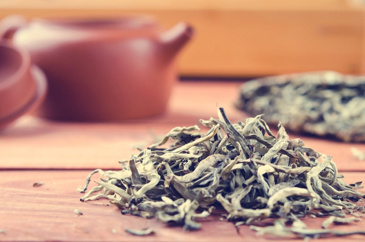 Loose white tea leaves on a wooden surface with teapot in background.