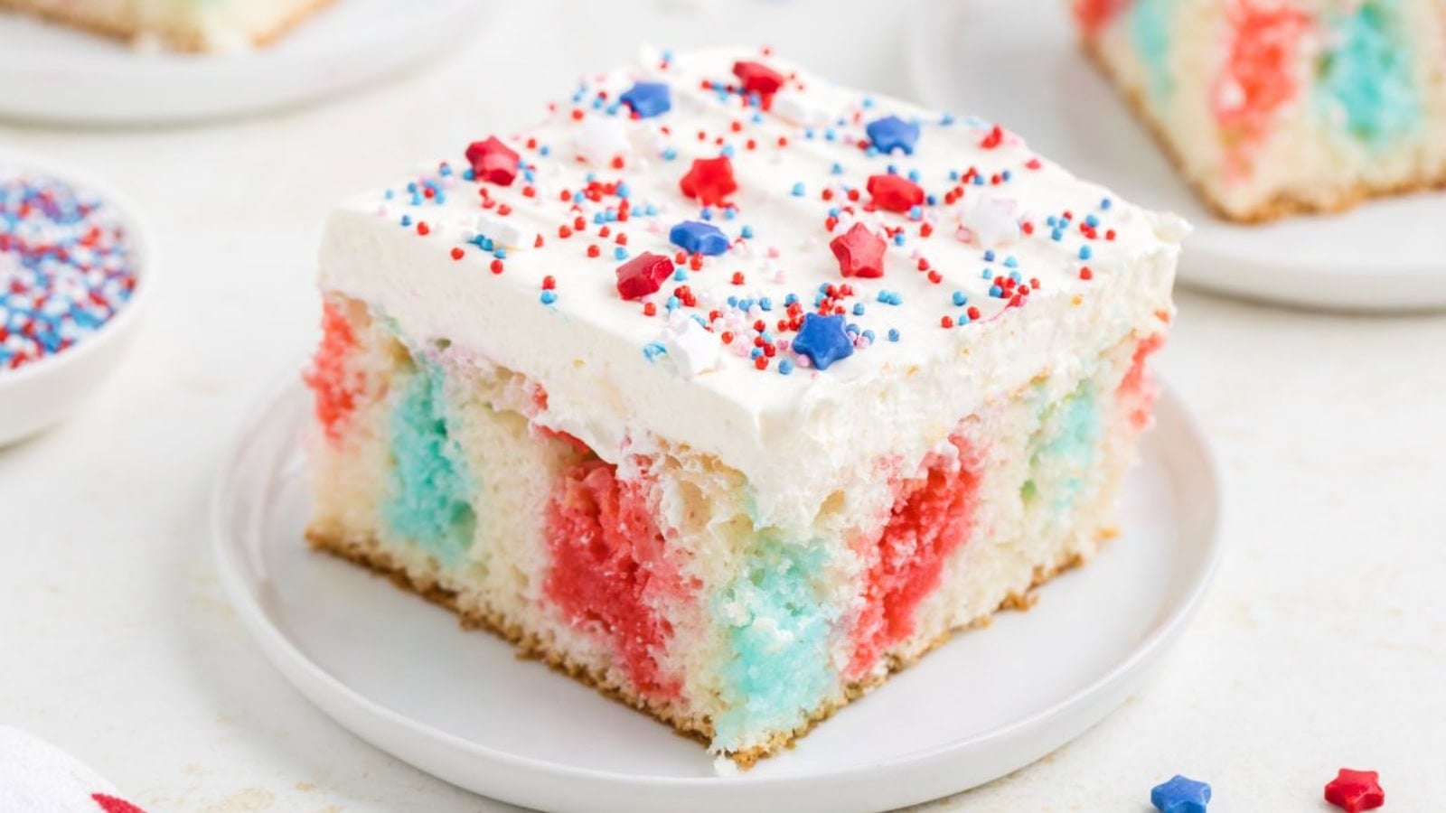 Jello poke cake with festive red and blue layers and whipped topping.