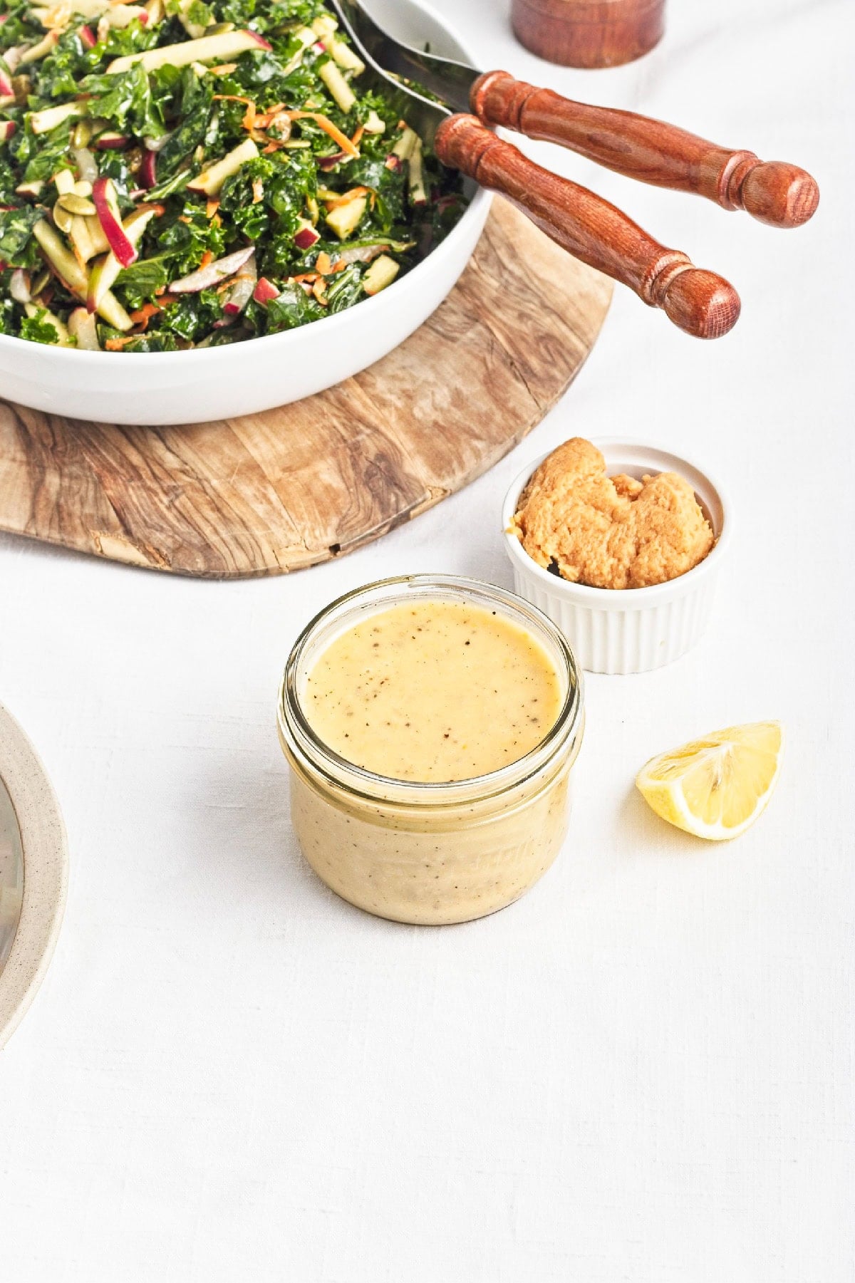 Creamy lemon miso dressing in a glass jar with miso paste and fresh lemon beside a kale salad.