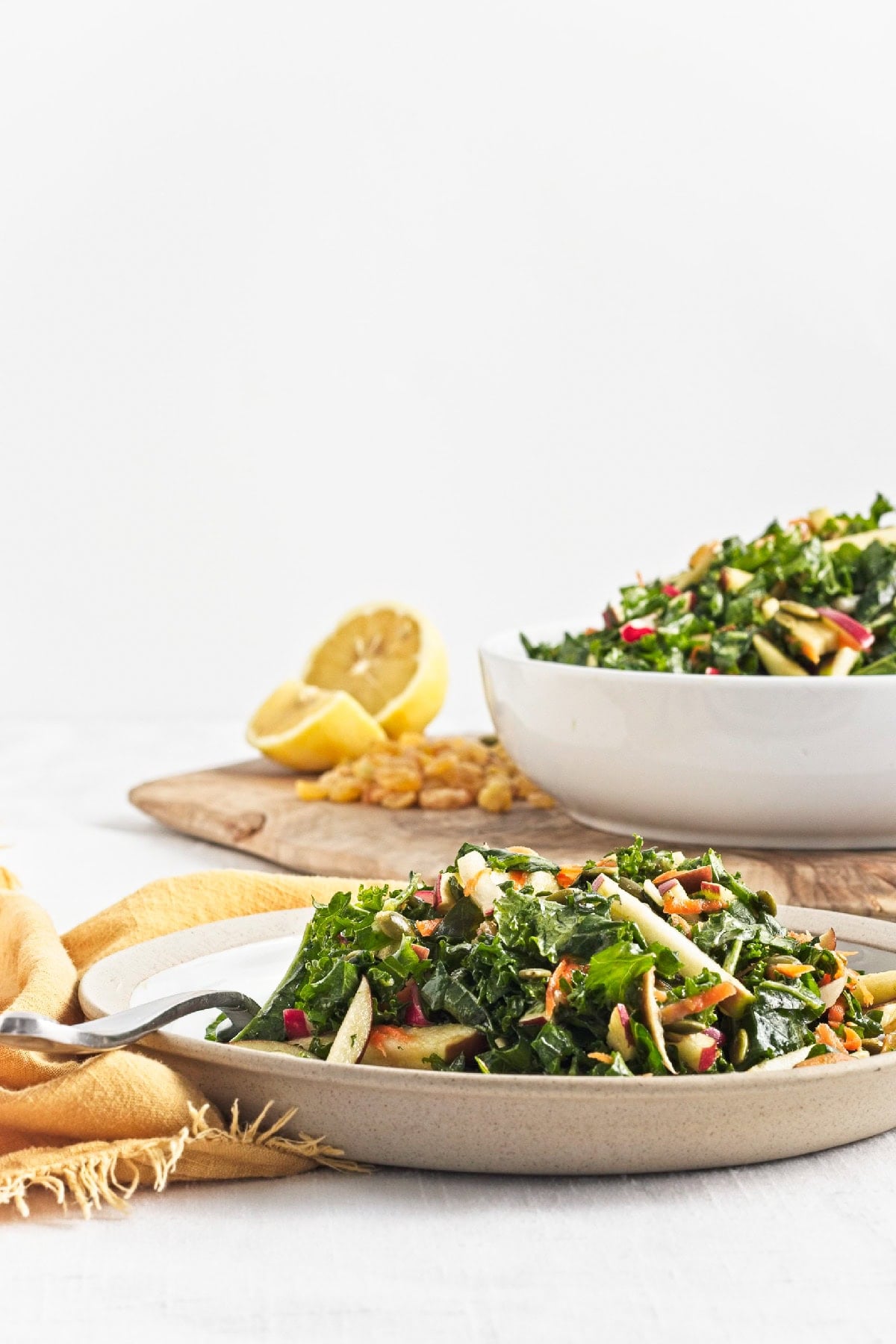 Plate of kale apple salad with crisp apples, carrots, radishes, and pumpkin seeds dressed in lemon miso dressing.
