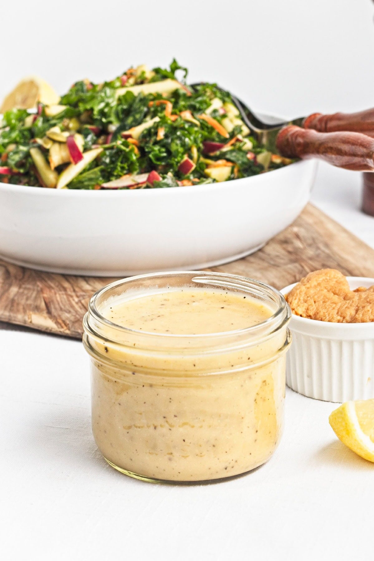 Close-up of lemon miso dressing in a glass jar served alongside fresh kale apple salad.