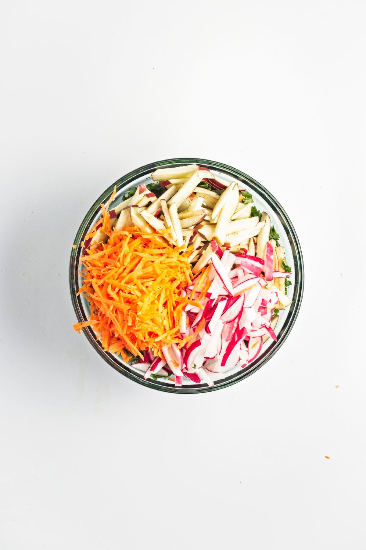 Julienned apples, shredded carrot, and sliced radishes prepared on a cutting board.