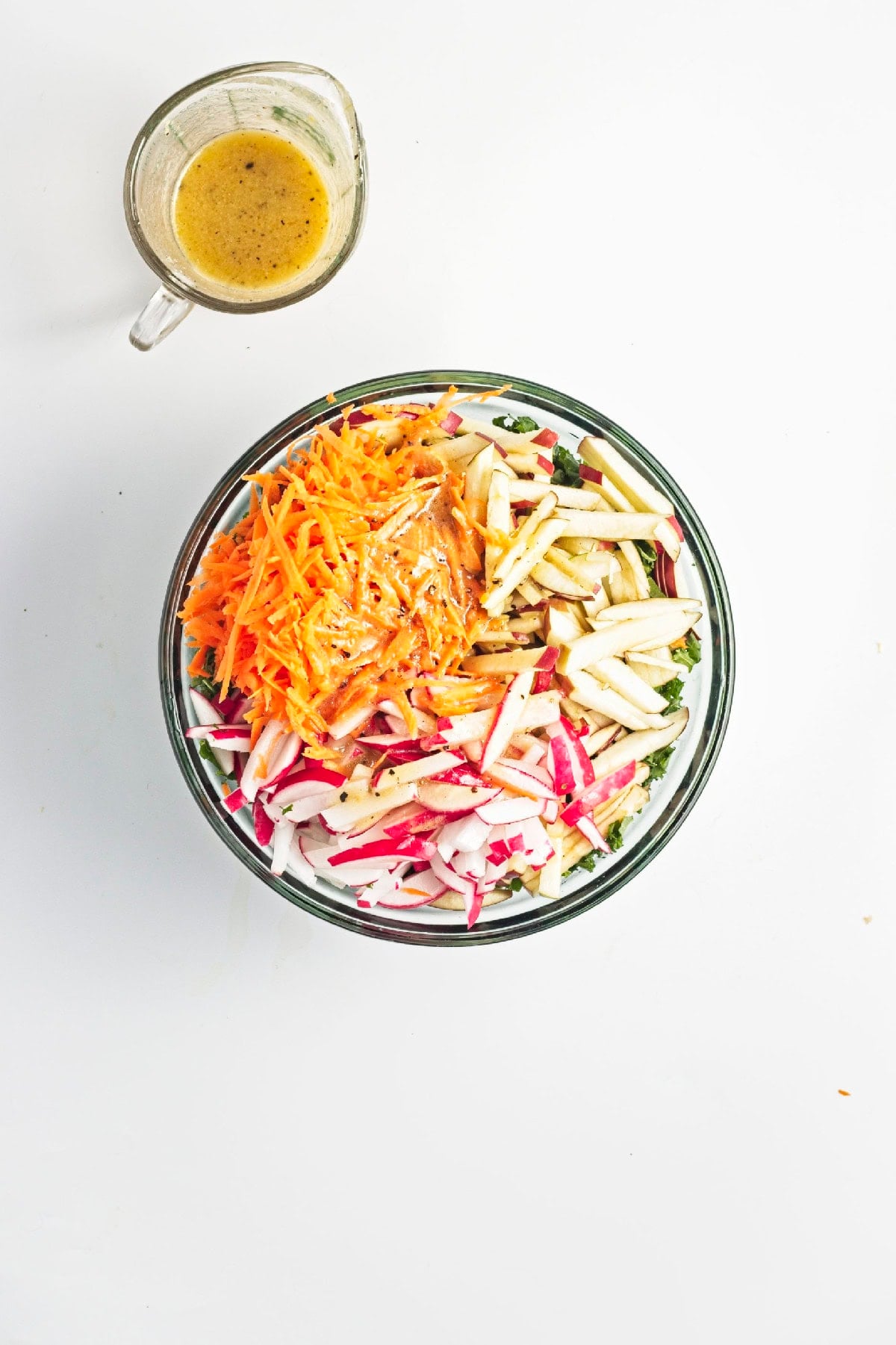 Chopped kale topped with apples, carrots, and radishes in a mixing bowl.