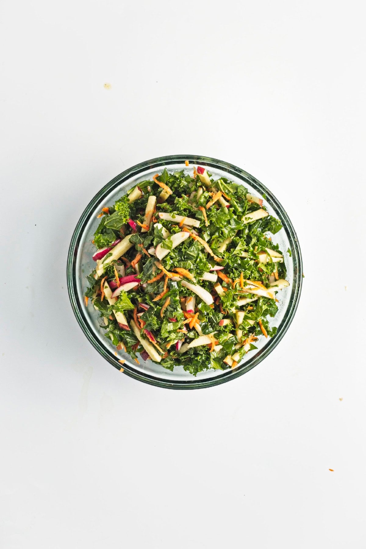 Lemon miso dressing poured over kale, apples, carrots, and radishes in a mixing bowl.
