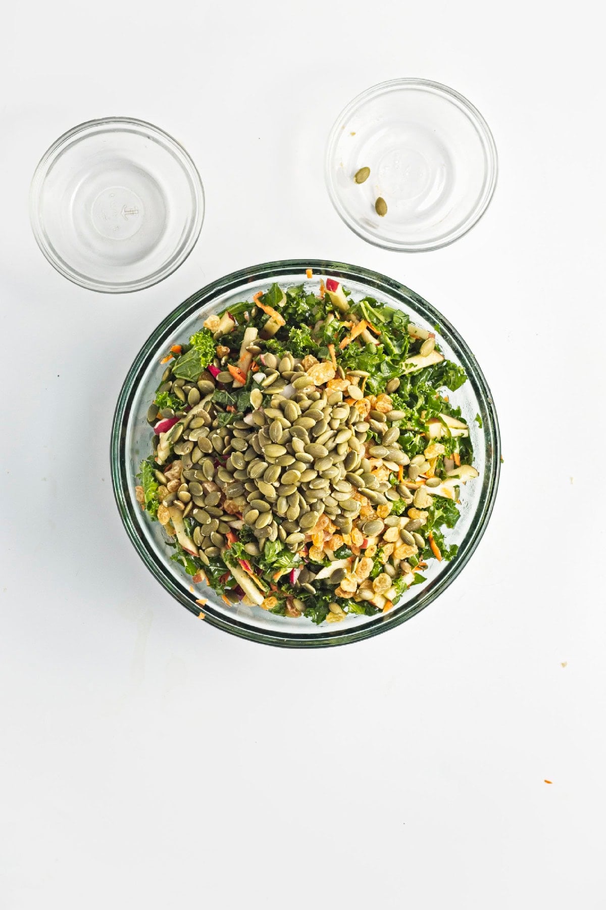 Kale salad tossed with dressing and topped with pumpkin seeds and raisins before serving.