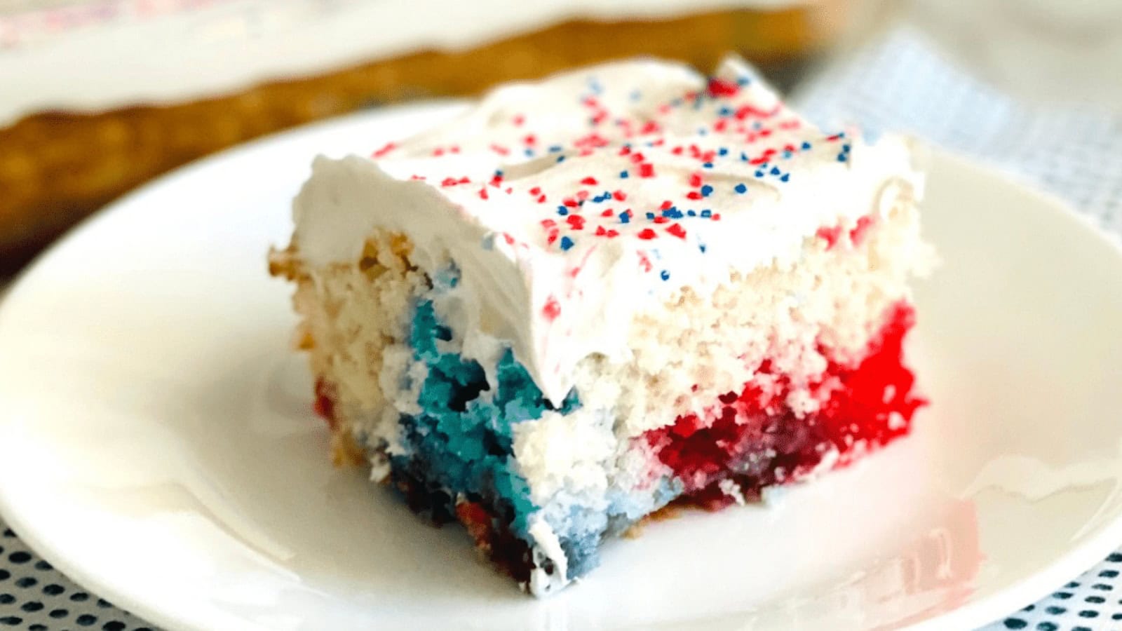 Red, white, and blue poke cake topped with whipped topping and berries.