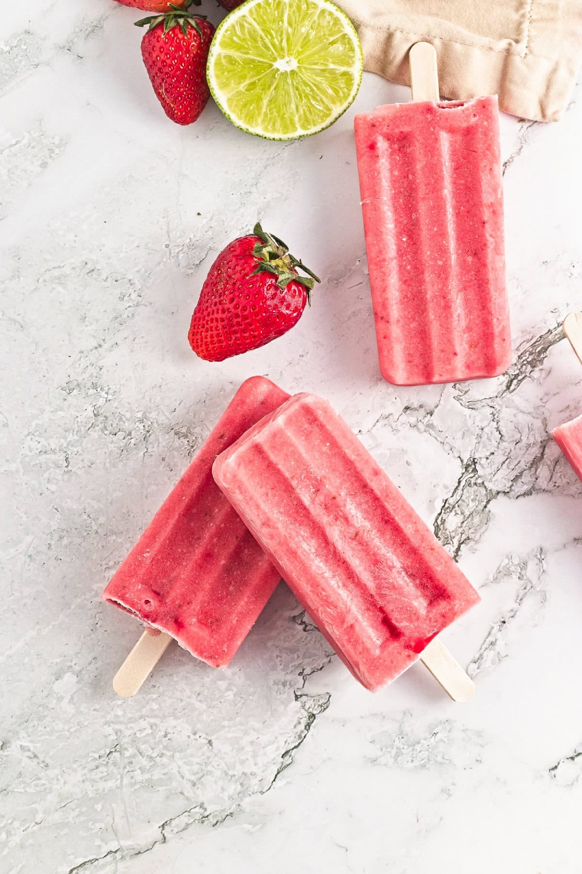 Homemade strawberry popsicles with fresh strawberries and sliced lime on a marble background.