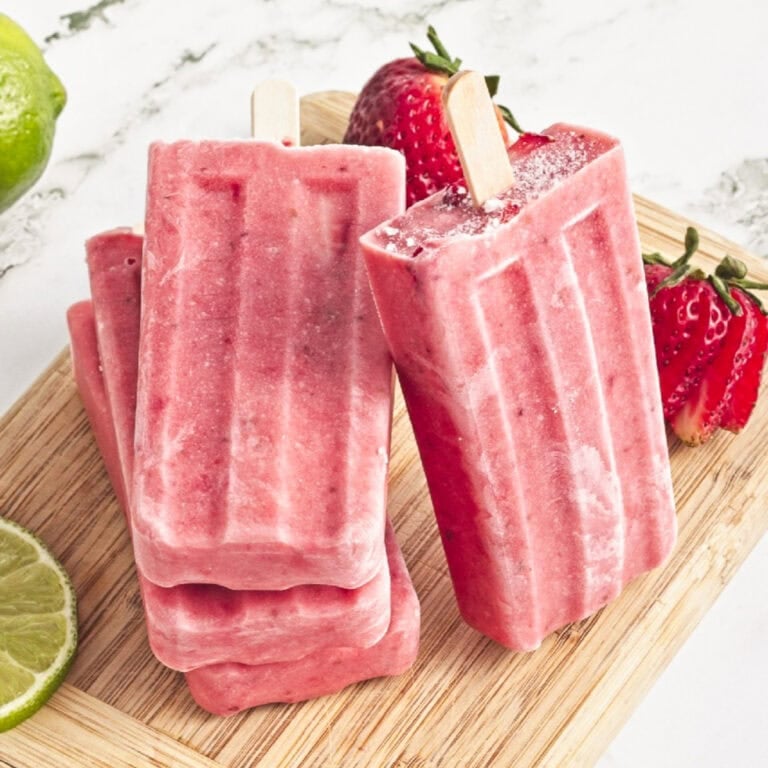 Homemade strawberry popsicles made with fresh strawberries, creamy coconut milk, and lime on a wooden board.