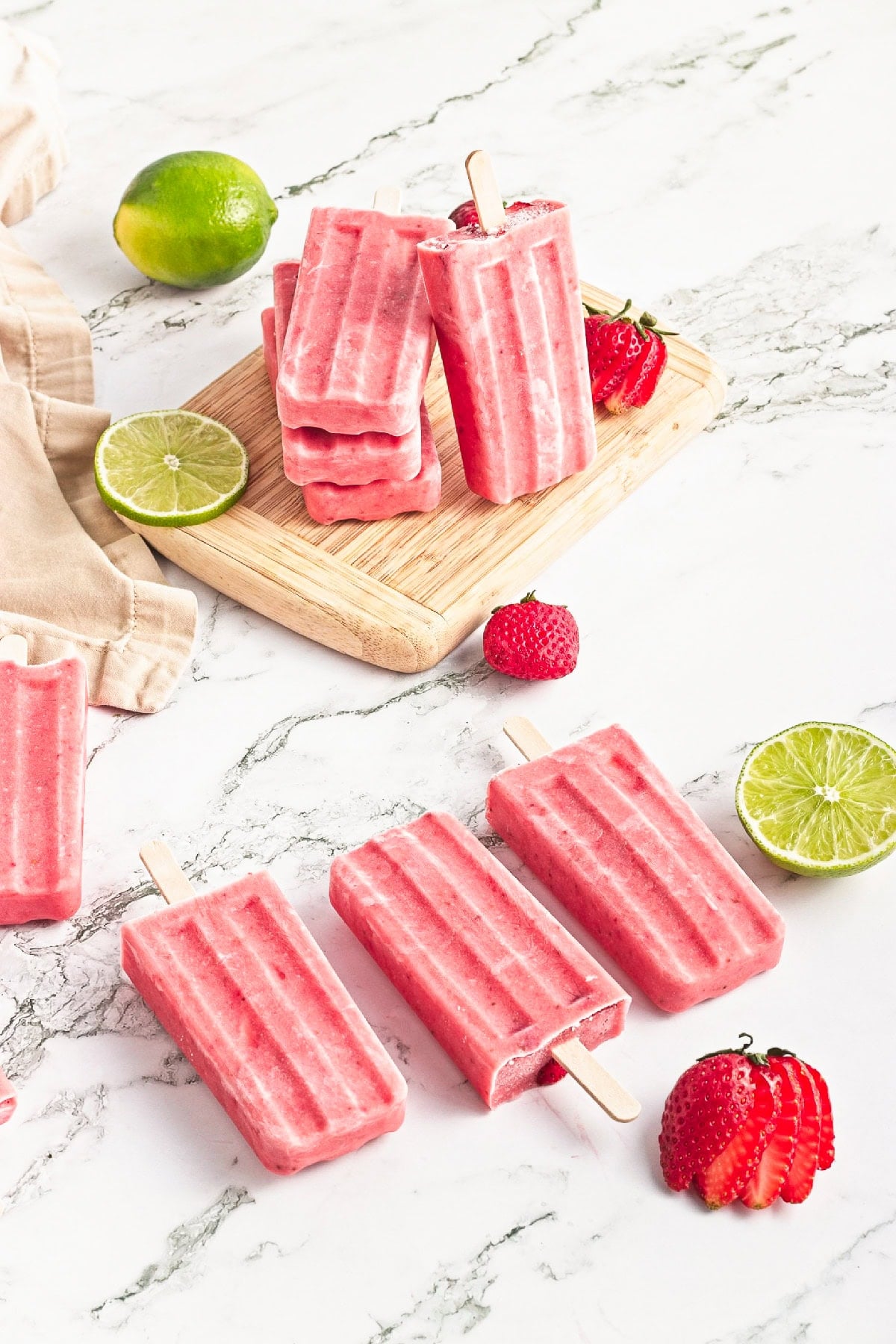Strawberry popsicles served on a wooden board with fresh strawberries and lime garnish.
