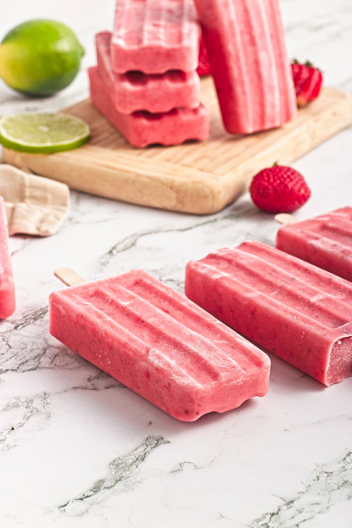 Close-up of creamy homemade strawberry popsicles on a marble countertop with fresh strawberries.