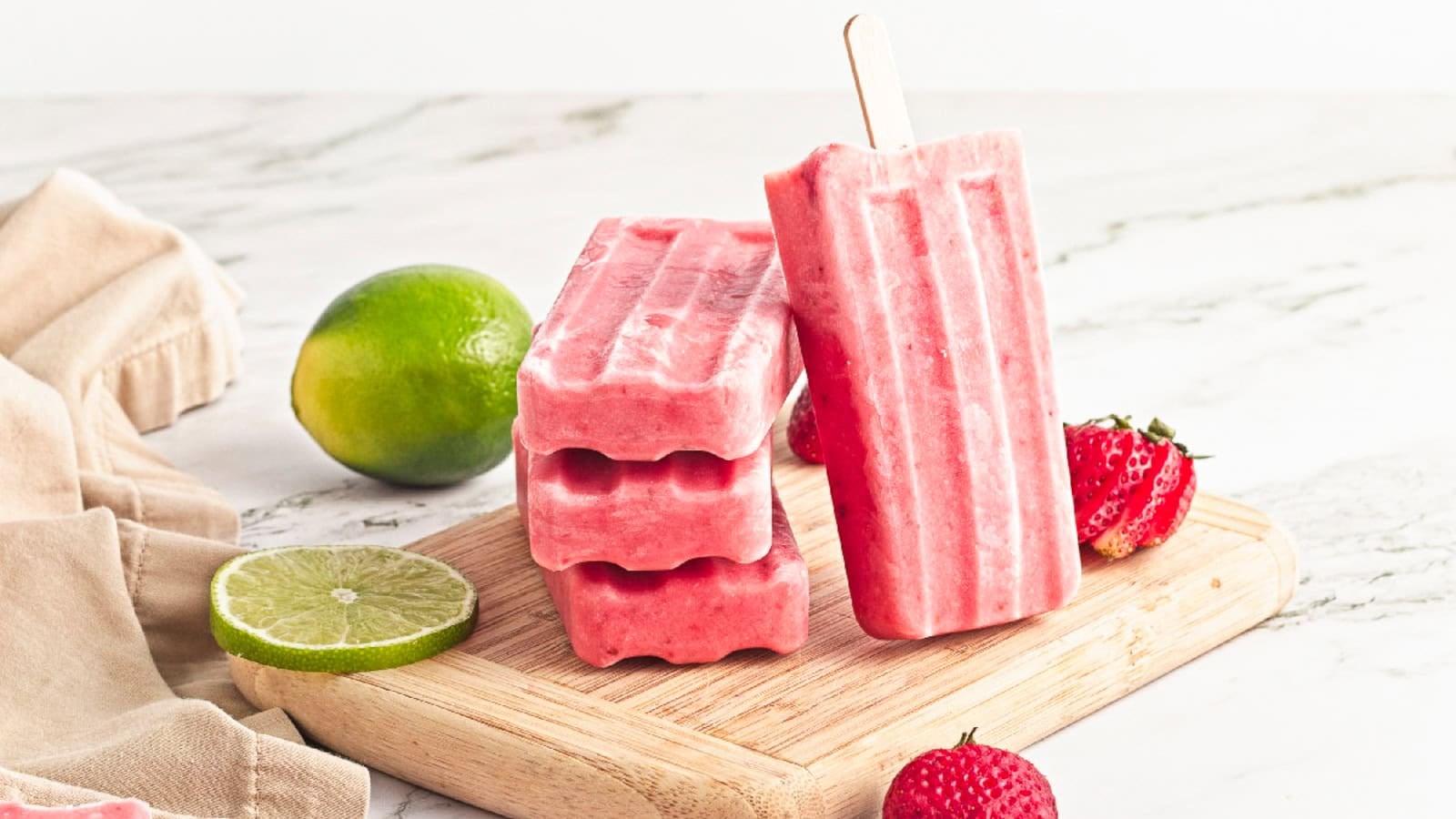 Easy strawberry popsicles with fresh strawberries and lime on a wooden cutting board, perfect for a refreshing summer dessert.