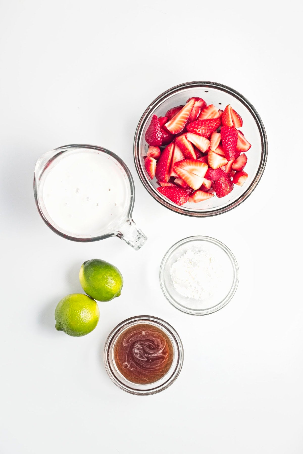 Ingredients for homemade strawberry popsicles including strawberries, coconut milk, maple syrup, cornstarch, and fresh limes.