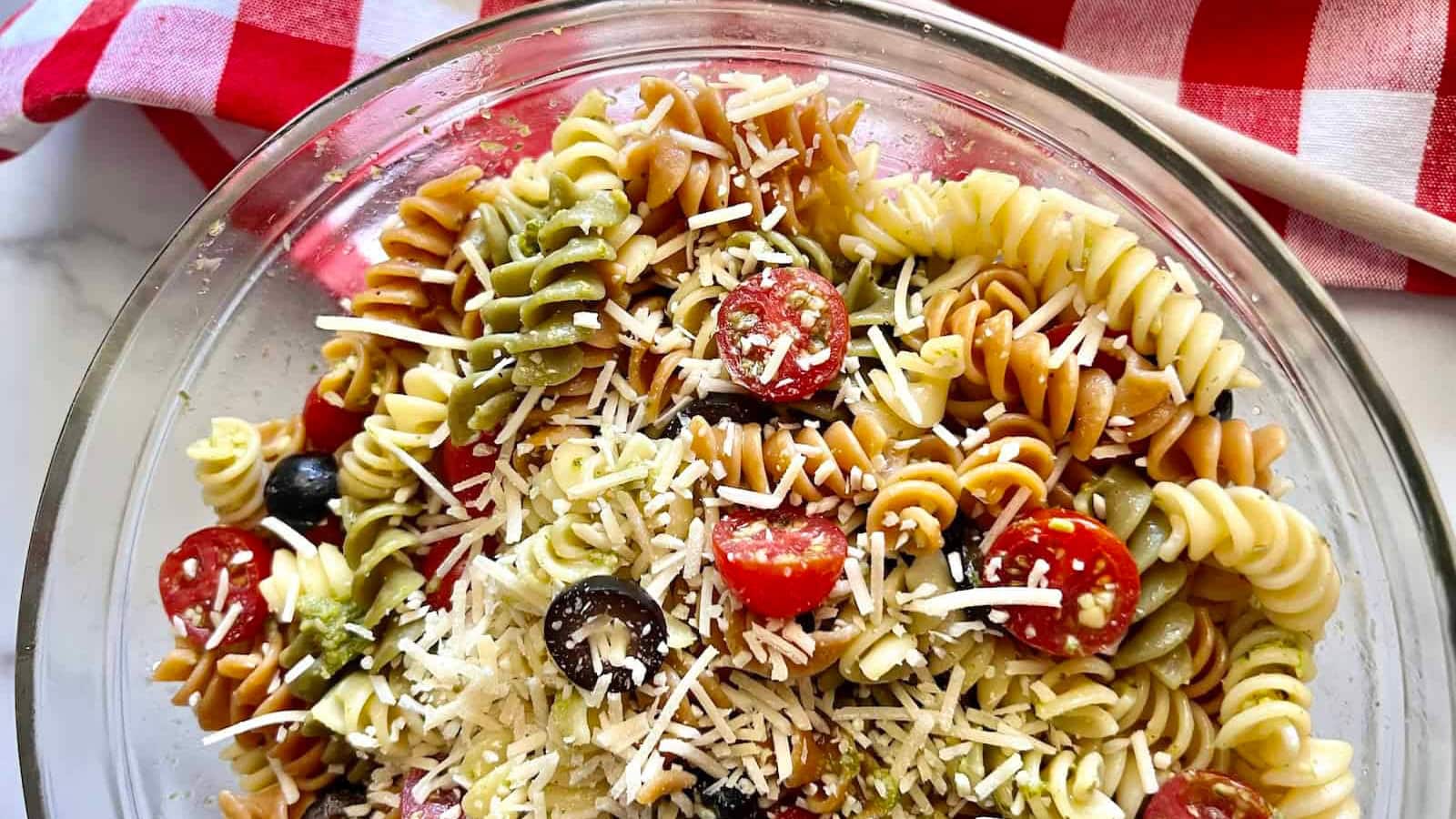 Pasta salad mixed with pesto, vegetables, and fresh herbs.