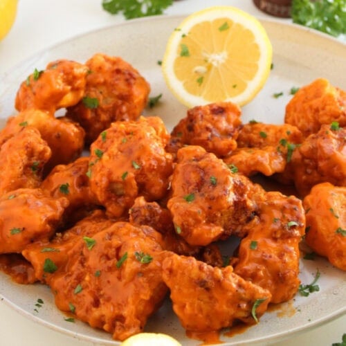 Boneless buffalo wings coated in spicy buffalo sauce on a plate with lemon wedges and celery.