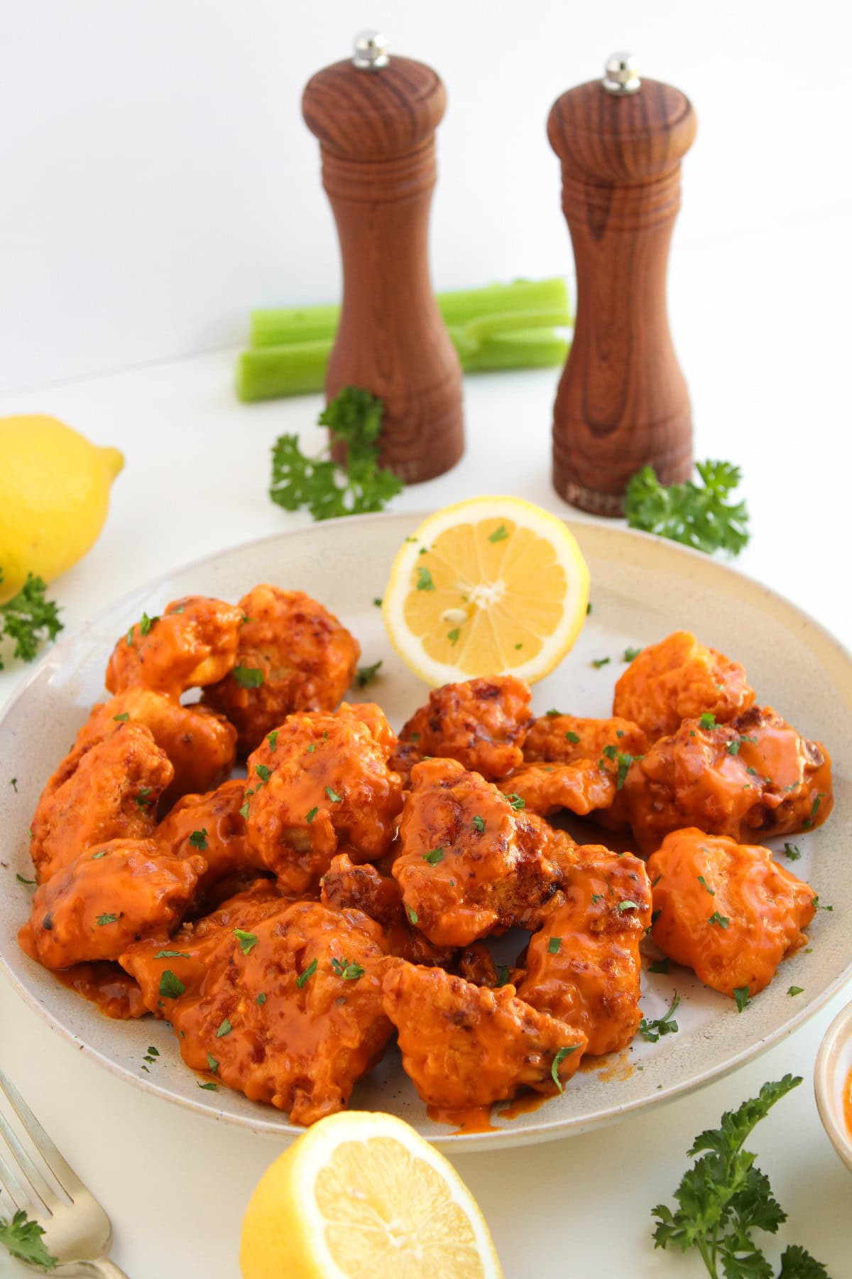 Boneless buffalo wings served on a plate with lemon slices, celery, and parsley garnish.
