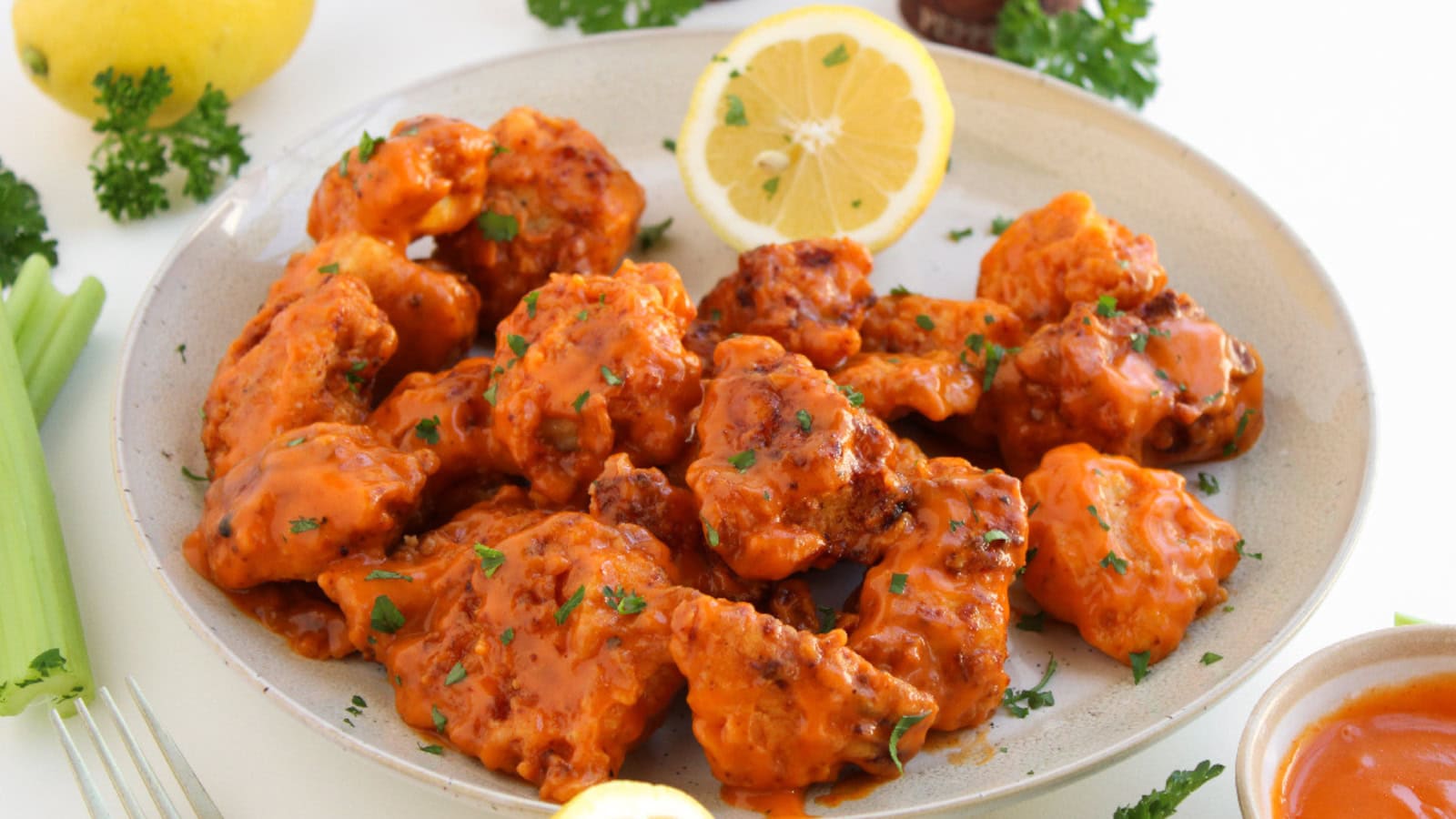 Plate of crispy boneless buffalo wings tossed in buffalo sauce with celery, lemon, and dipping sauce.