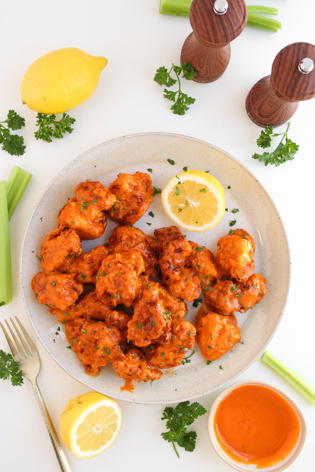 Overhead view of crispy boneless buffalo wings coated in buffalo sauce with celery, lemon, and dipping sauce.