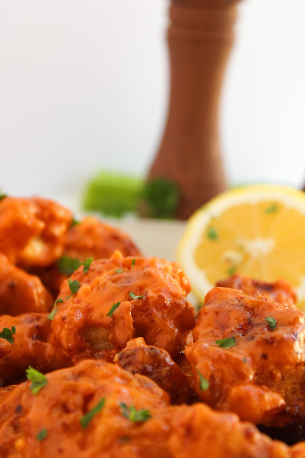 Macro shot of saucy boneless buffalo wings with lemon and celery in the background.