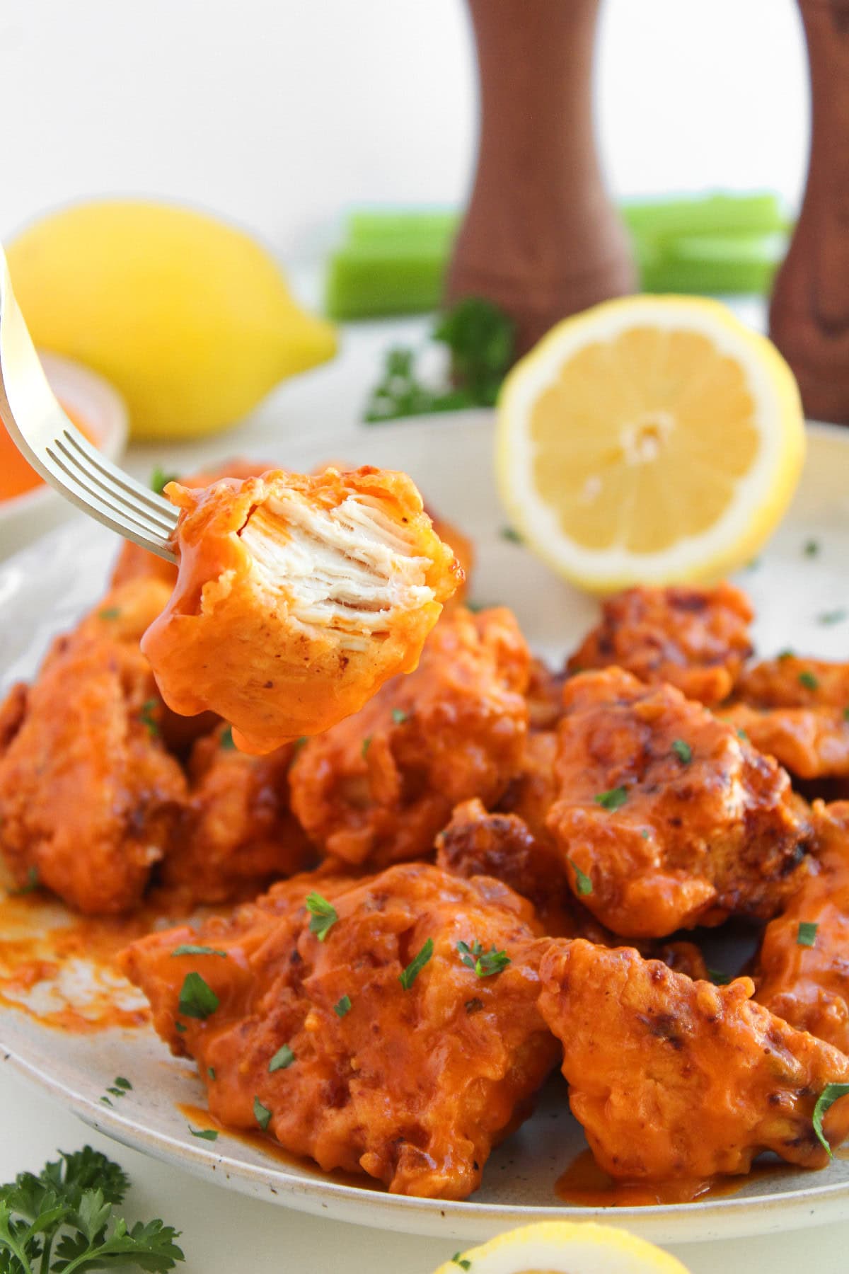 Piece of boneless buffalo wing on a fork showing juicy chicken coated in buffalo sauce.