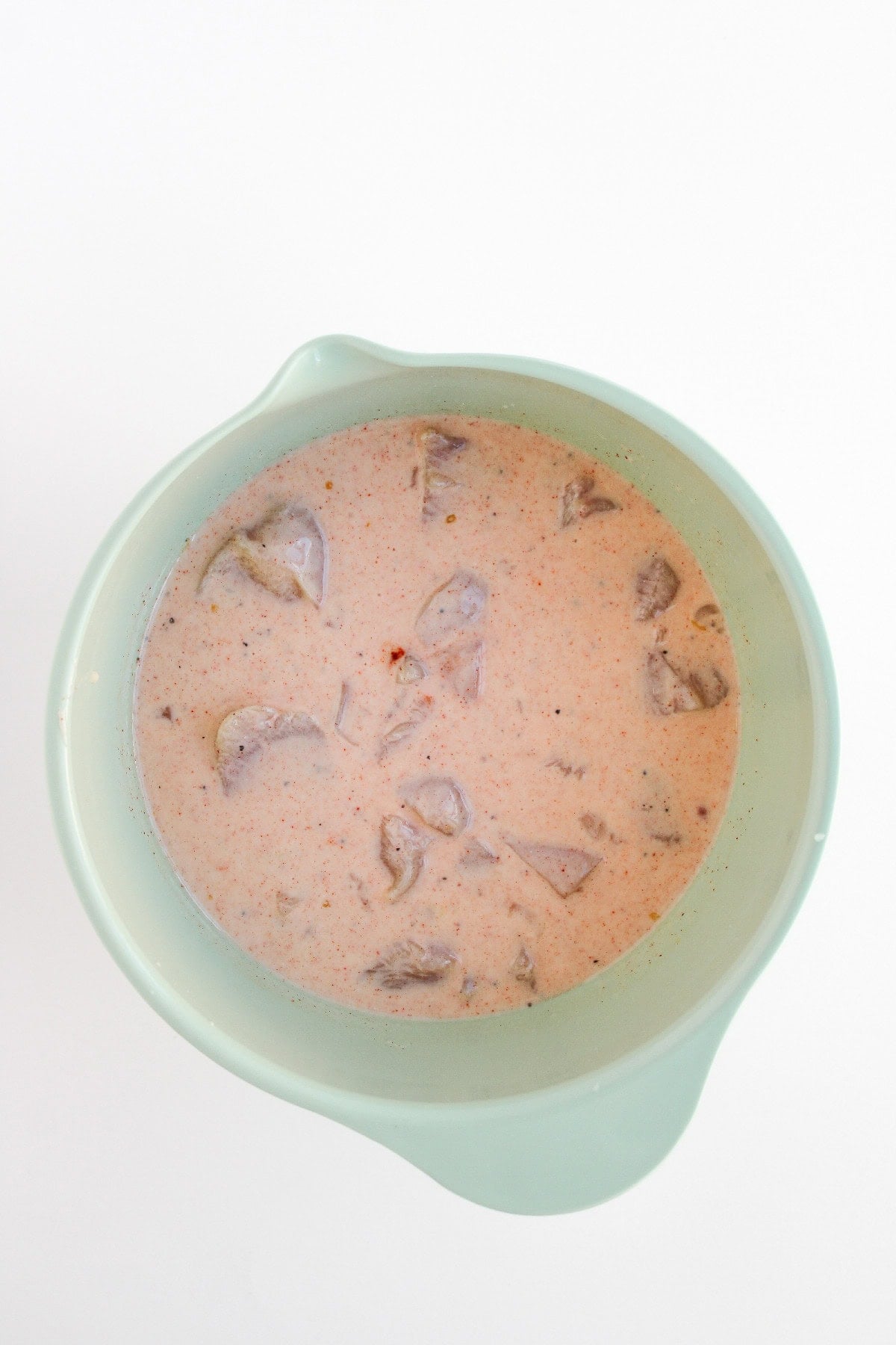 Chicken pieces soaking in a seasoned buttermilk marinade for boneless buffalo wings.