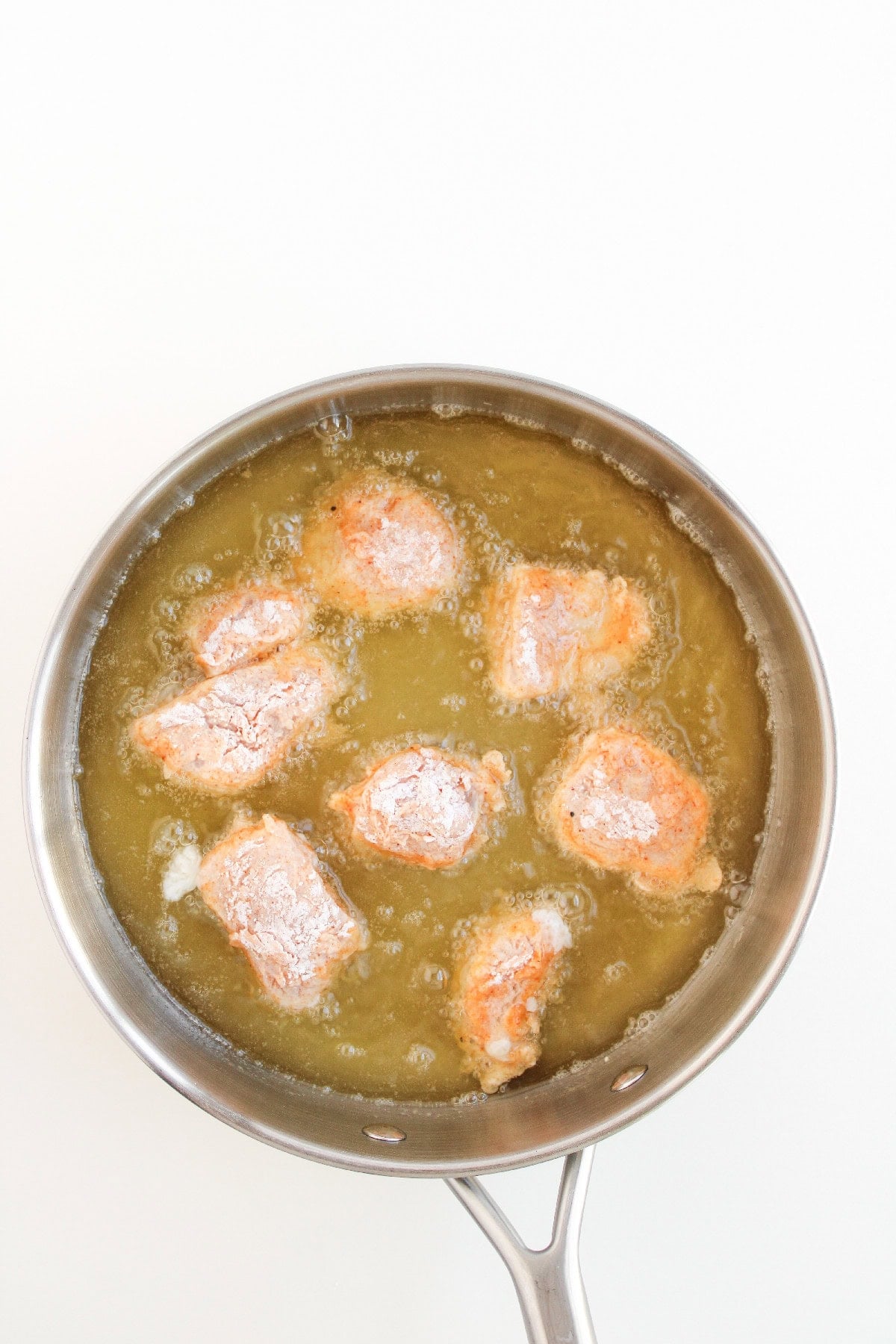 Breaded chicken pieces frying in hot oil for boneless buffalo wings.