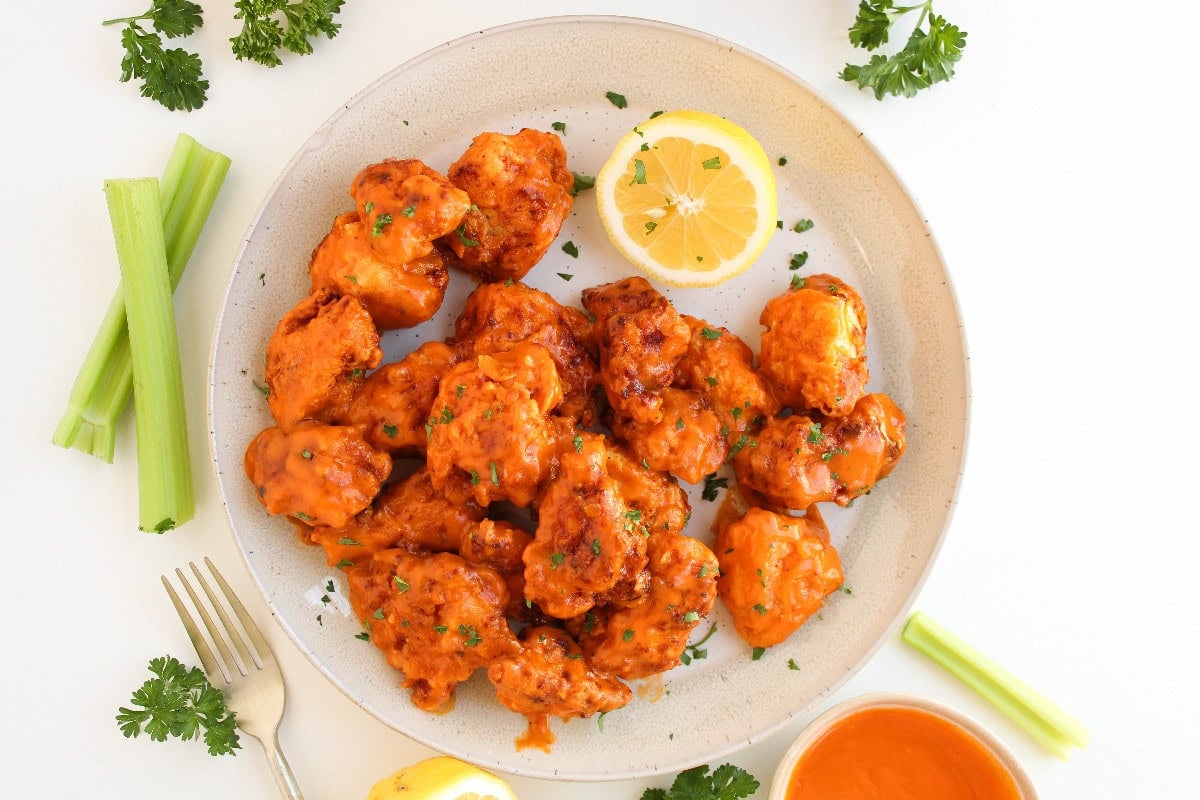 Overhead view of crispy boneless buffalo wings coated in buffalo sauce with celery and lemon.