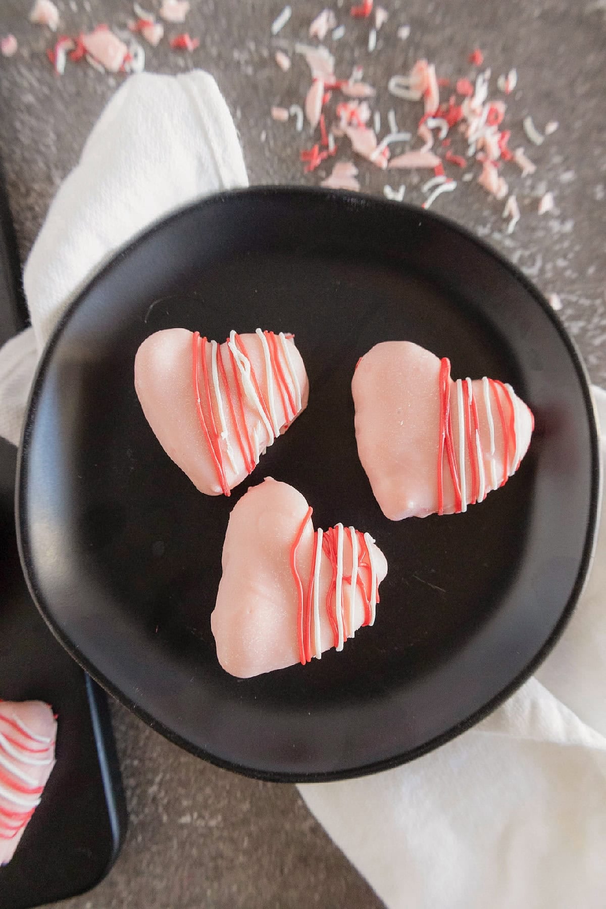 Three pink heart-shaped cake truffles with red and white drizzle served in a black bowl.