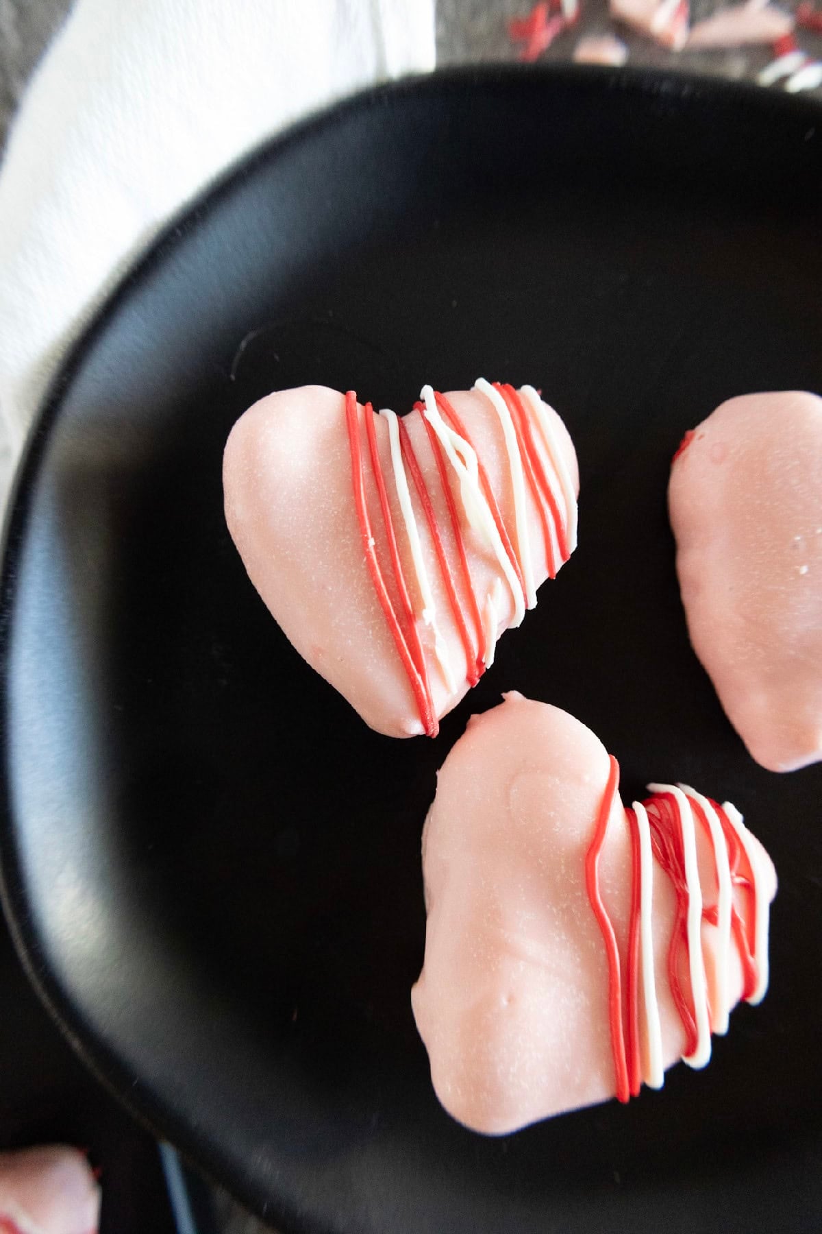 Close-up of pink heart-shaped cake truffles decorated with red and white candy drizzle.