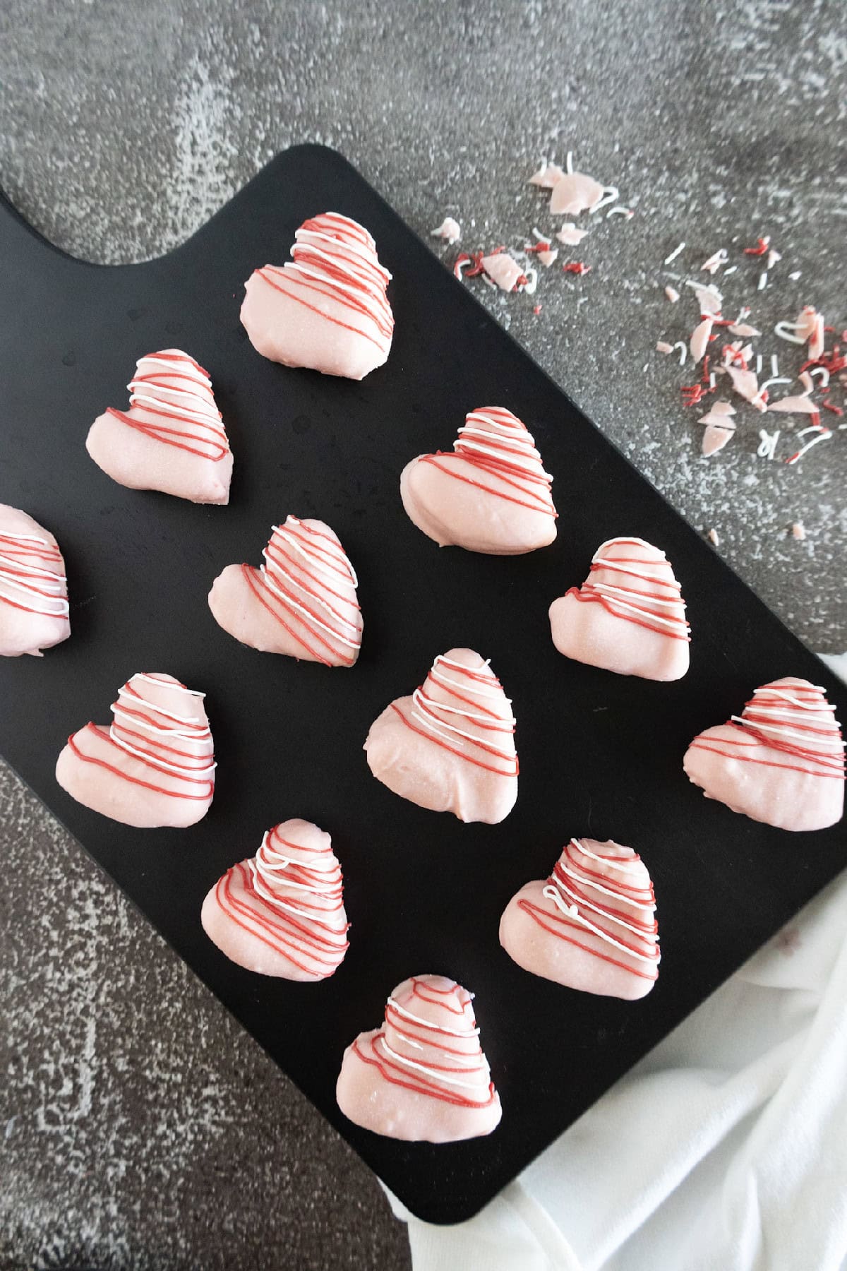 Pink heart-shaped cake truffles arranged on a black serving tray with red and white drizzle.
