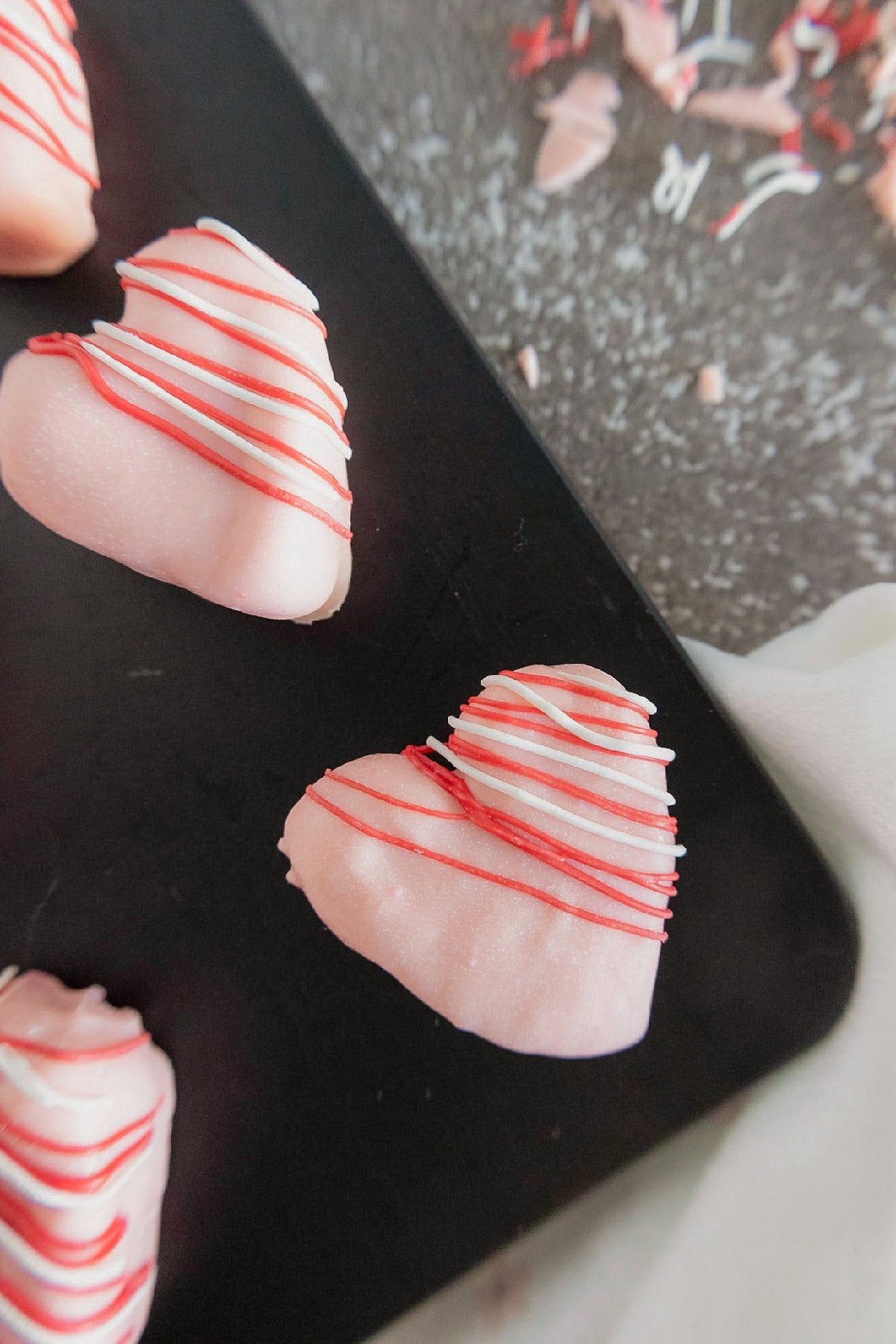 Close-up of a pink heart-shaped cake truffle with red and white drizzle on a black tray.