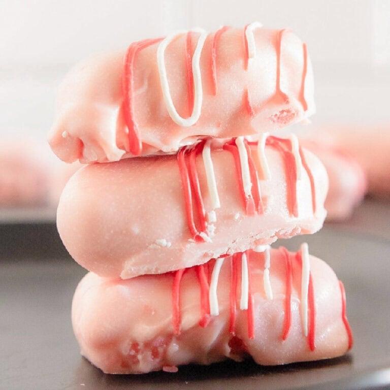 Stack of three pink cake truffles coated in candy melts and drizzled with pink and white chocolate on a black plate.