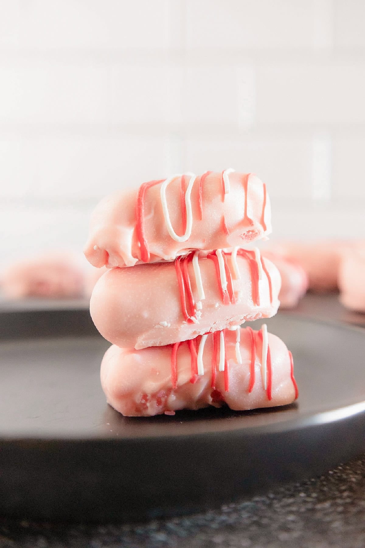 Stack of three pink cake truffles coated in candy melts and drizzled with red and white chocolate.
