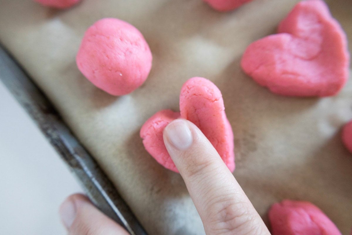 Finger pressing the center of a pink cake truffle to shape it into a heart.