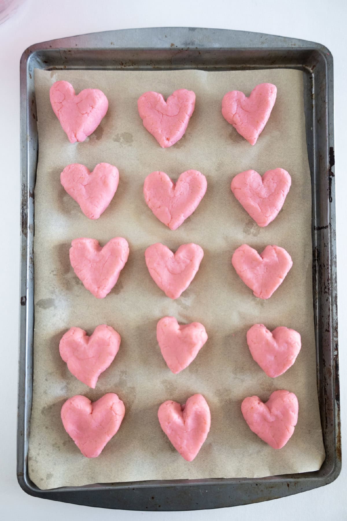 Pink heart-shaped cake truffles arranged on a parchment-lined baking sheet before being coated in candy melts.