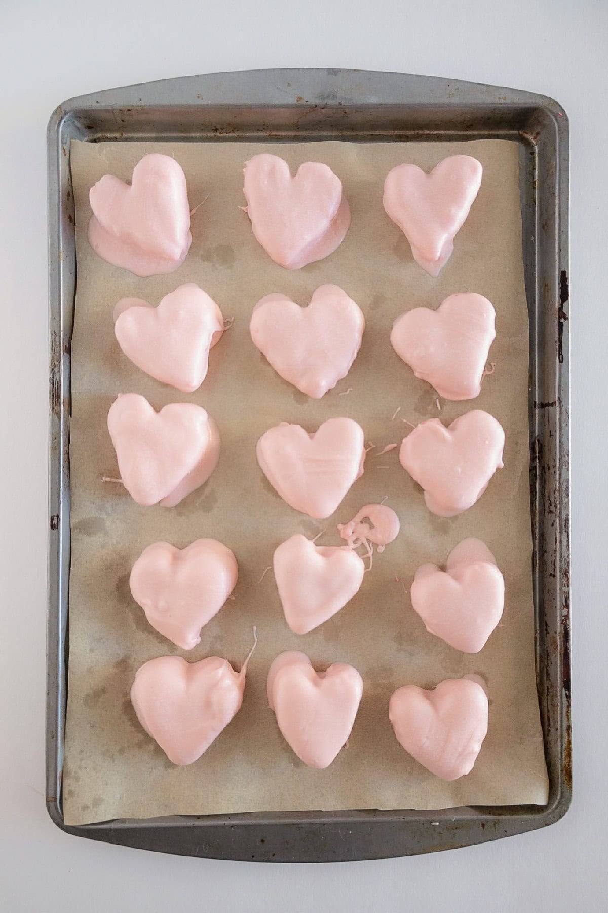 Heart-shaped cake truffles coated in pink candy melts and resting on a parchment-lined baking sheet.