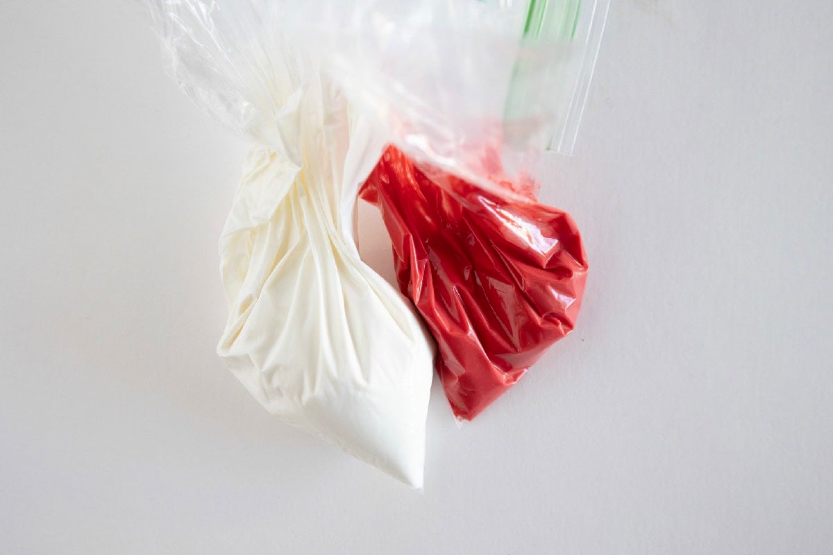 Melted white and red candy coating in piping bags ready for drizzling.