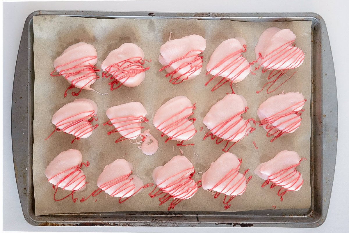 Pink heart-shaped cake truffles drizzled with red candy coating on a parchment-lined baking sheet.