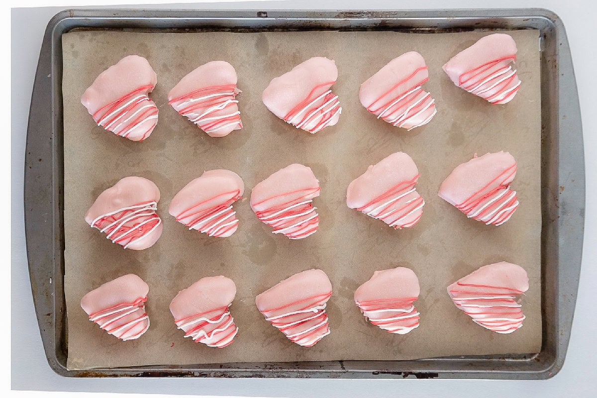 Finished pink heart-shaped cake truffles with red and white drizzle cooling on a parchment-lined baking sheet.