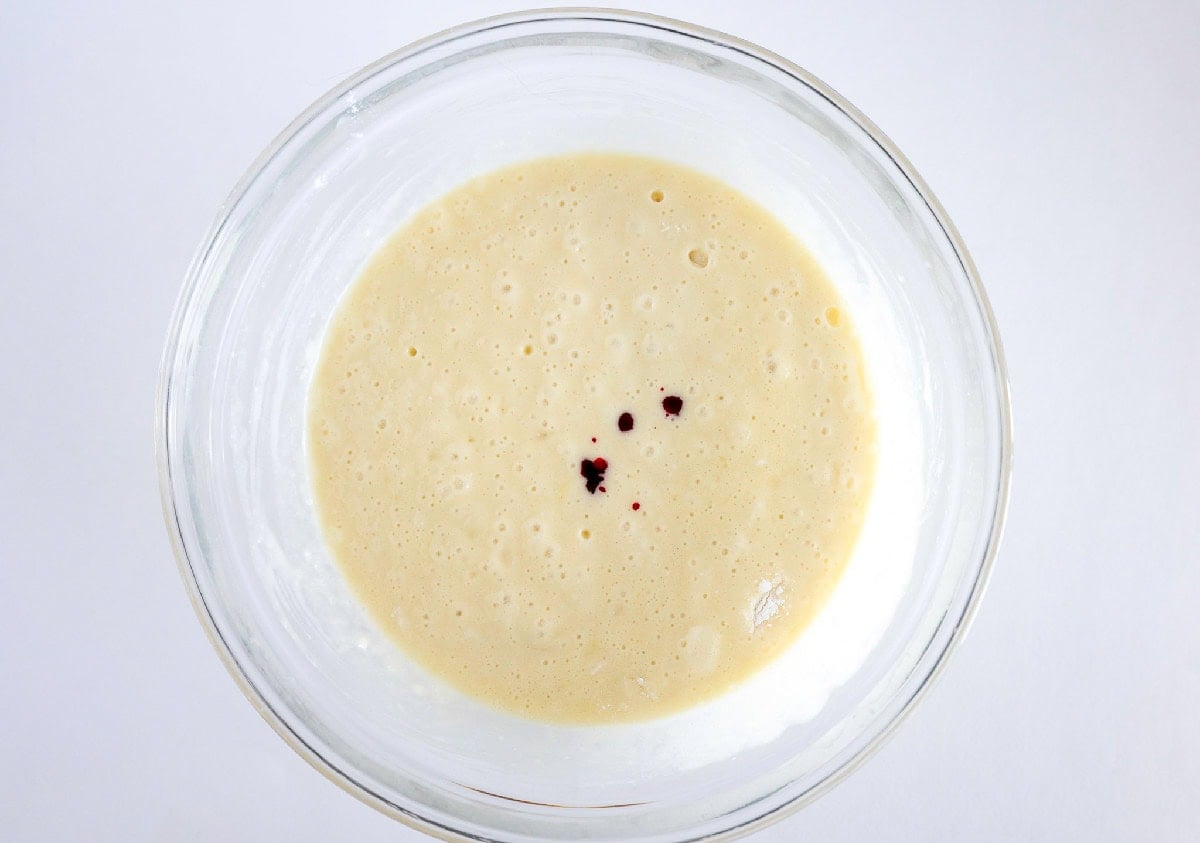 Pink food coloring added to cake batter in a glass bowl.