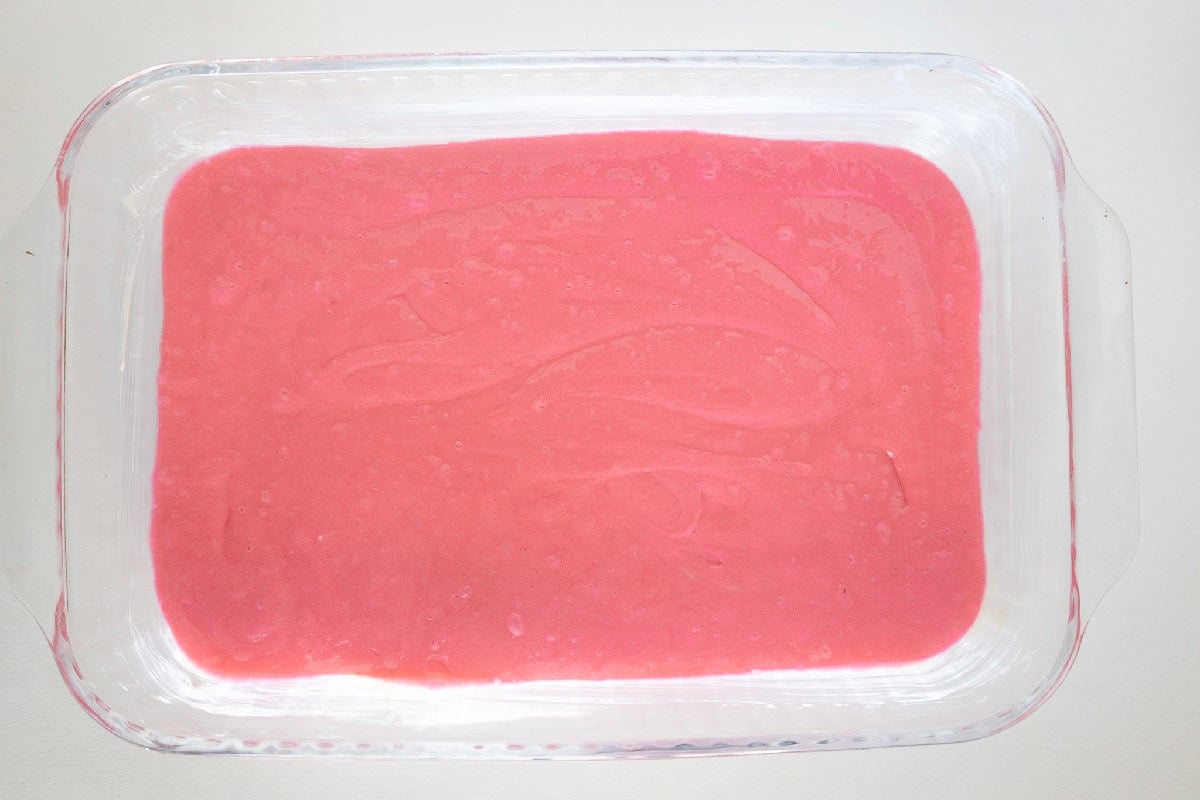 Pink cake batter spread evenly in a greased glass baking dish before baking.