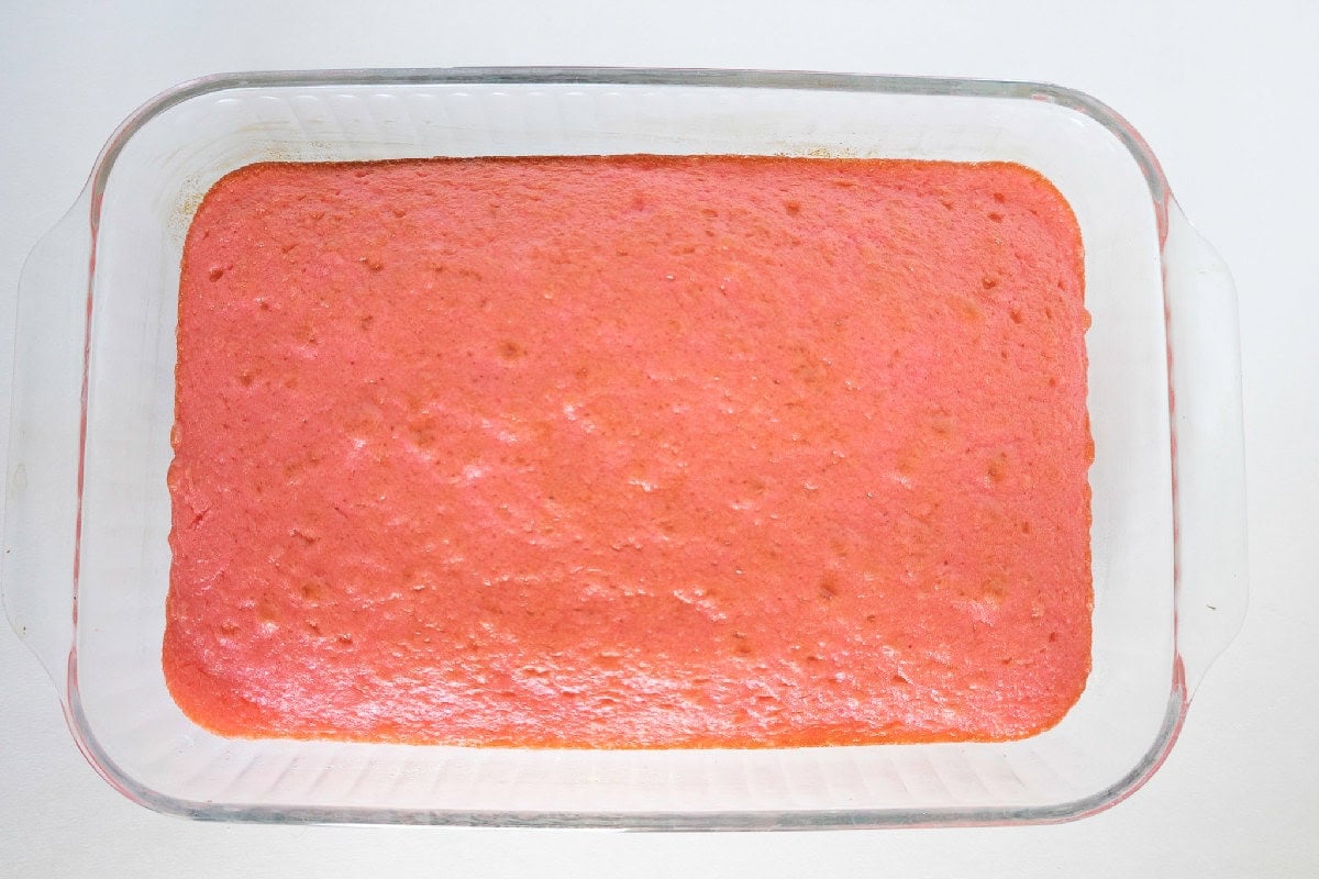 Baked pink cake cooling in a glass baking dish.