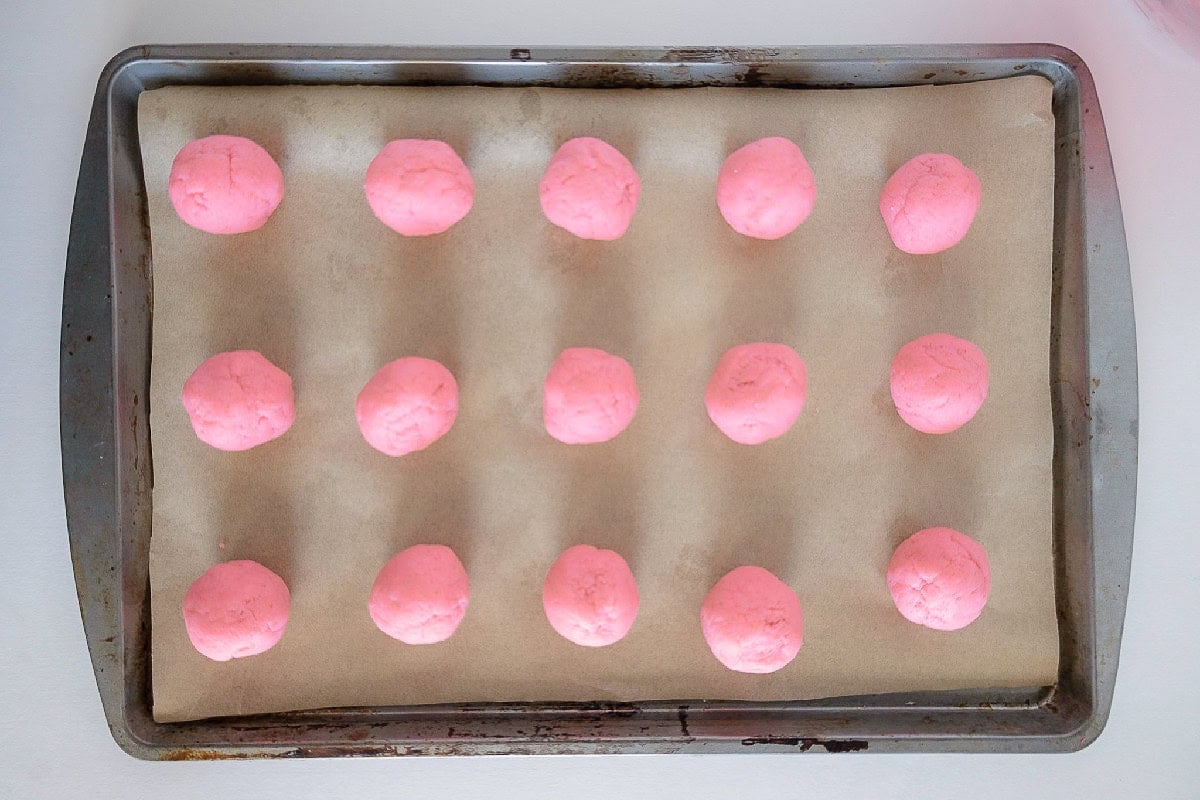 Pink cake truffle balls arranged on a parchment-lined baking sheet.